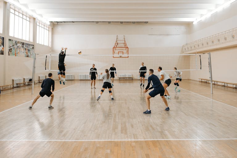 Team players engaging in a dynamic indoor volleyball match on a wooden court.